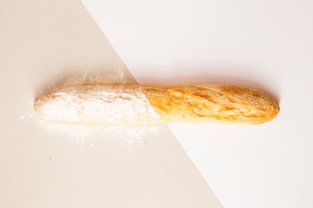 Ein Baguette auf der einen Hälfte roh und mit Mehl bestäubt, auf der anderen Seite schon goldgelb gebacken