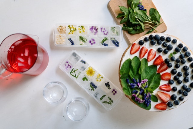 Ein mit Früchten dekorierter Kuchen und Eiswürfel mit Blüten daneben