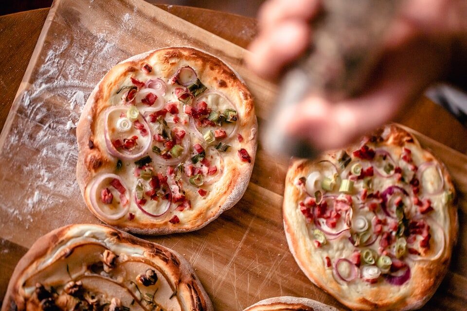 Eine Person würzt vier Elsässer Flammkuchen