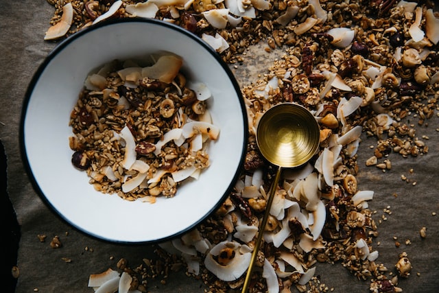 Eine Schüssel mit trockenen Zutaten für Müsli, ein Löffel und noch mehr Zutaten daneben.