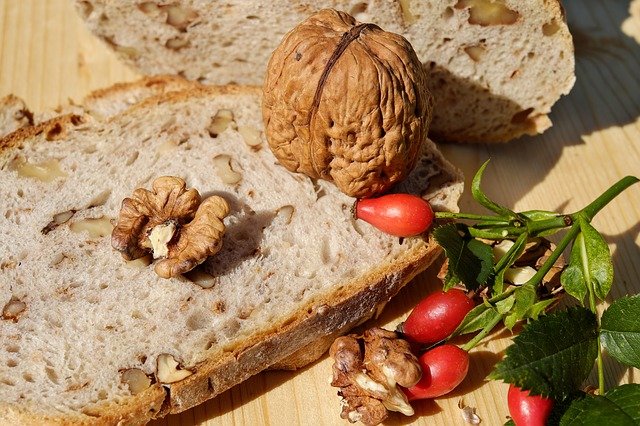 Eine Brotscheibe mit Walnüssen und Hagebutten liegt auf einem Holztisch