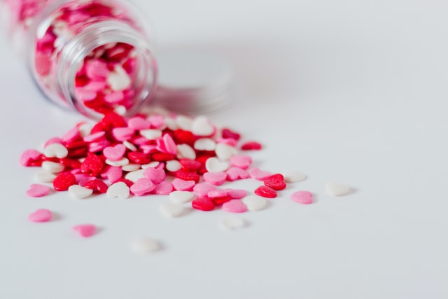 Kleine rote, pinke und weiße Herzen kommen aus einem umgeschütteten Glas.