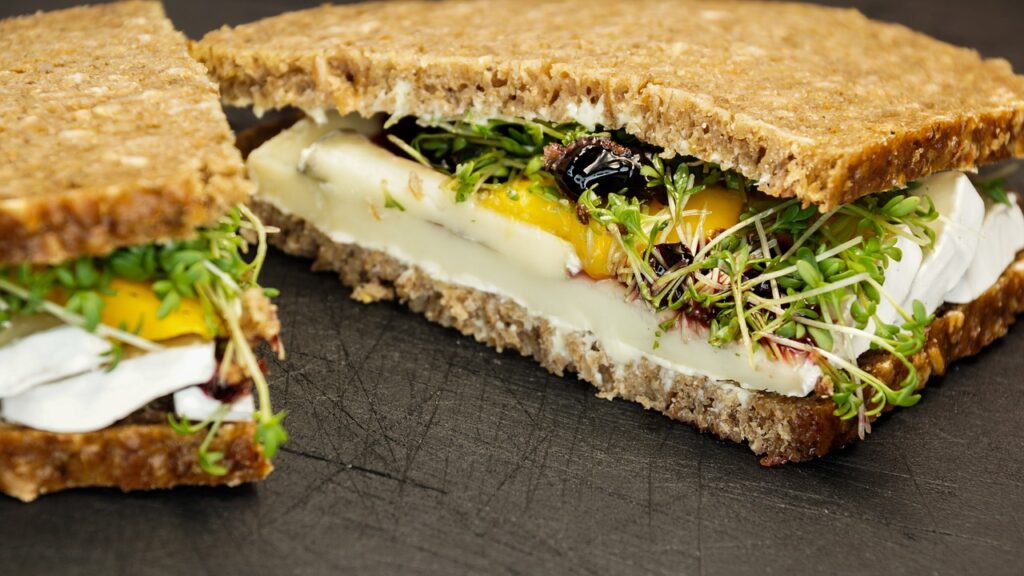 Auf einem dunklen Untergrund liegen zwei Pumpernickel-Schnitten belegt mit Kresse, Käse und Orangen.