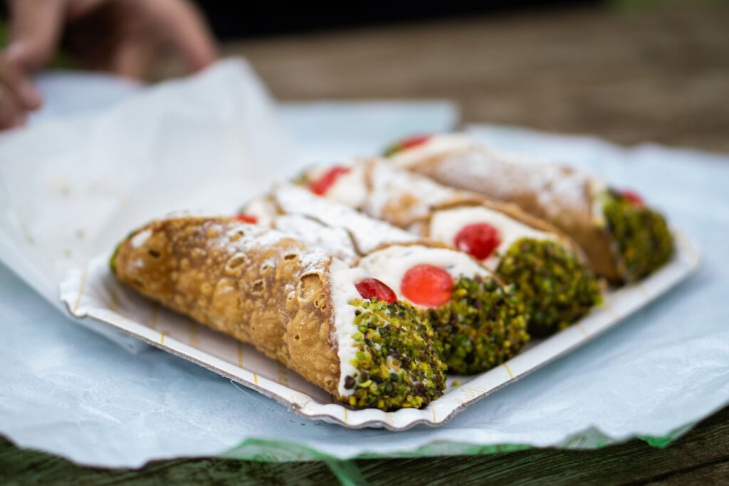 Vier Cannoli mit einer Cremefüllung, Pistazien und Desserkirschen werden serviert