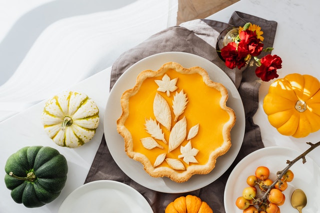 Ein Kürbiskuchen mit Teig in Form von Blättern als Deko, inmitten von bunten Kürbissen