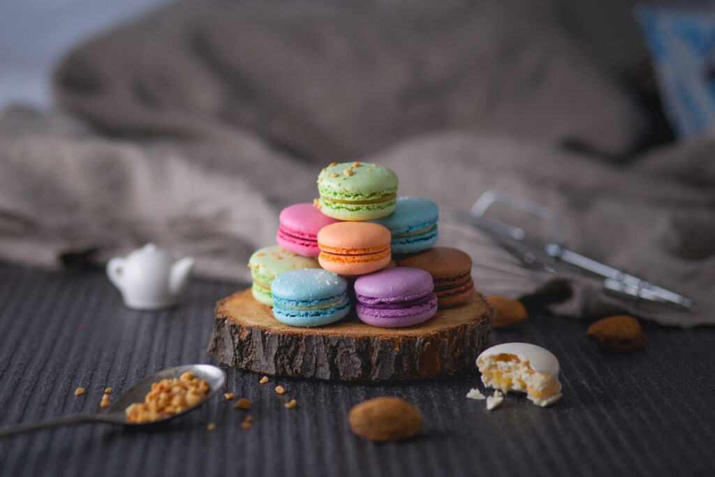 Ein Stapel aus bunten Macarons liegt auf einer Baumstammscheibe