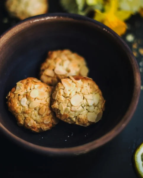 Drei Mandelkekse mit Mandelblättchen auf einem terrakottafarbenen Teller, dekoriert mit gelben und weißen Narzissen.