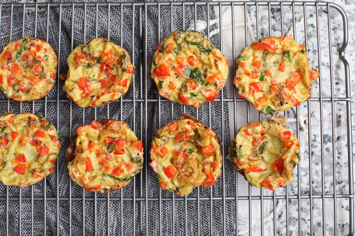 Einige herzhafte Muffins gefüllt mit Tomate, Ei und Schnittlauch liegen nebeneinander auf einem Backblech.
