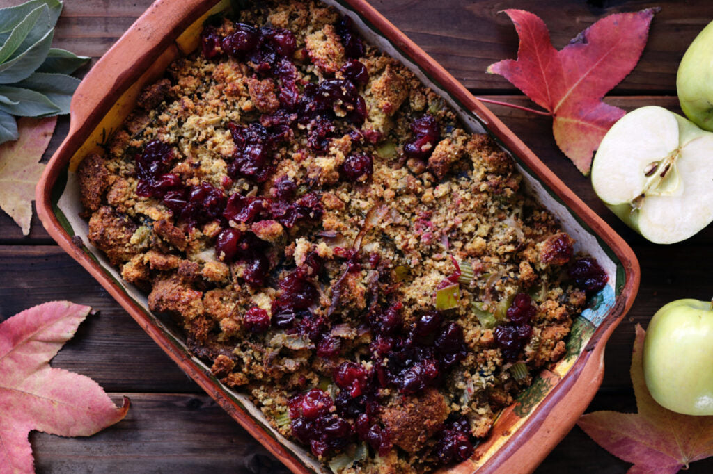 In einer Keramikform wurde ein Rhabarber-Crumble mit Kirschen gebacken. Ringsherum liegen gefärbte Blätter und Äpfel