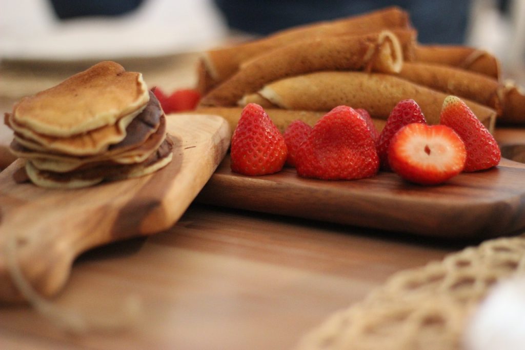 Auf zwei Schneidebrettern sind zum einen Pancakes und zum anderen Eierkuchen mit Erdbeeren serviert.