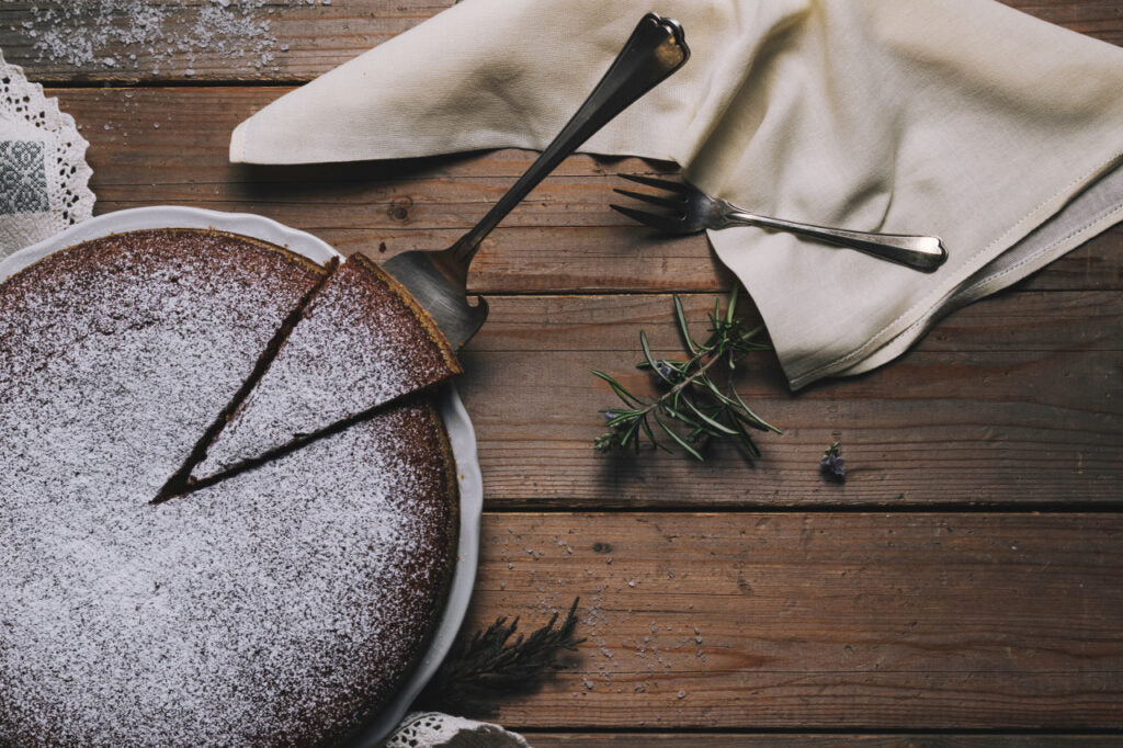 Ein winterlicher, mit Puderzucker dekorierter Kuchen steht auf einem Holzboden zusammen mit Tischdecken, Servietten und Tannenzweigen
