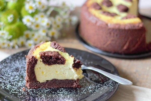 Ein Stück Zupfkuchen auf einem Teller mit Puderzucker und Gabel. Dahinter steht der Rest des Kuchens und ein paar Blumen.
