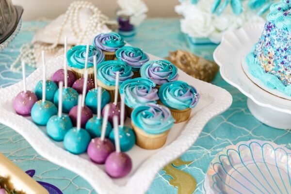 Auf einem Teller stehen Cake Pops und Muffins mit lila-blauem Frosting