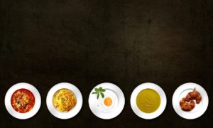 Auf einer schwarzen Fläche sind 5 Teller mit verschiedenen Speisen angerichtet. Von links nach rechts: Eine Nudelsuppe, Spagetti Carbonara, Spiegelei, eine cremige Suppe und Croissants.