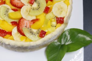 Ein Früchtekuchen ist mit Kiwis, Bananen, Erdbeeren und Pfirsichen dekoriert