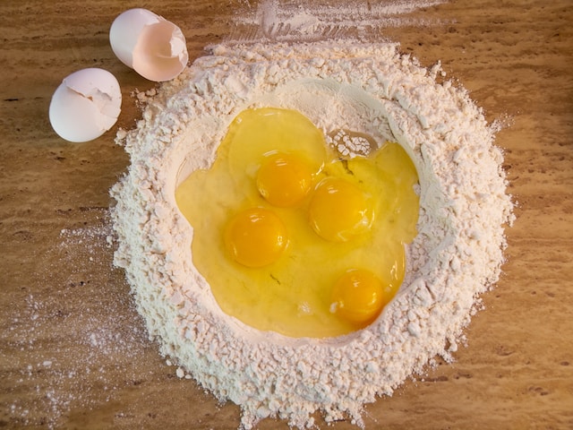 Aufgeschlagene Eier schwimmen in einem Kreis aus Mehl, die Schalen liegen daneben 