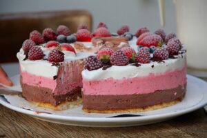 Ein Eiskuchen mit Schichten aus Schokoladen-, Erdbeer- und Vanilleeis, darauf angefrostete Früchte.