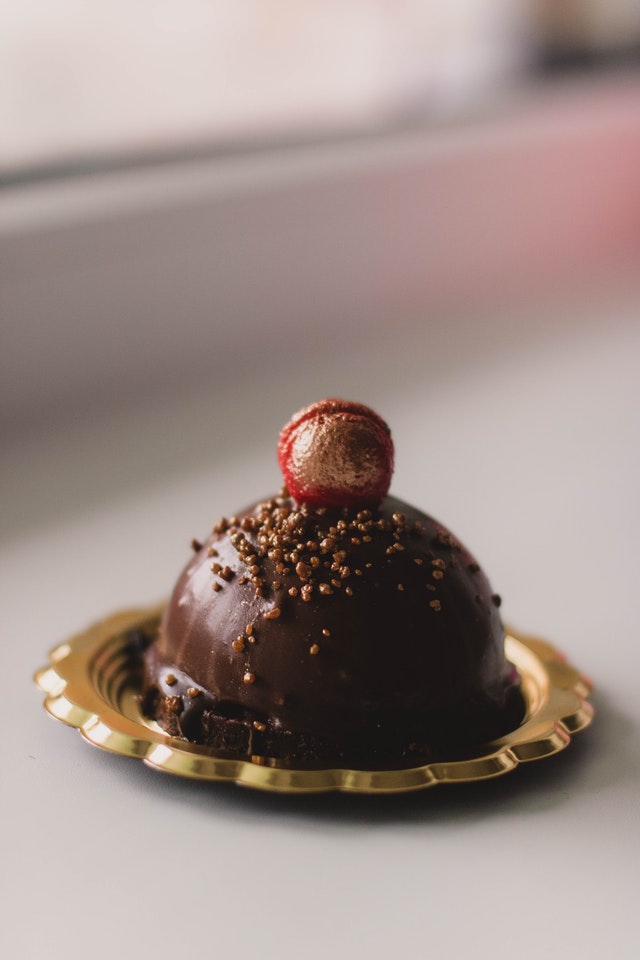 Eine kleine Eisbombe mit Schokoladenüberzug liegt auf einem goldenen Teller