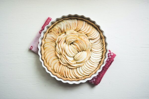 Eine weiße Keramik-Tarteform in der sich ein ungedeckter Kuchen mit Äpfeln zum Backen befindet