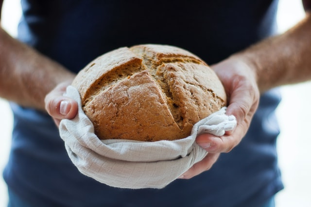 Jemand hält ein Brot mit einem Küchentuch ringsherum in der Hand