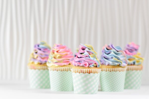 Fünf Cupcakes mit einem bunten Frosting stehen vor einem weißen Vorhang