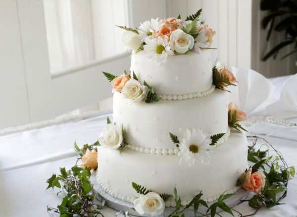 Eine weiße Hochzeitstorte dekoriert mit Fondant und einer Menge Blumen steht auf einem Tisch