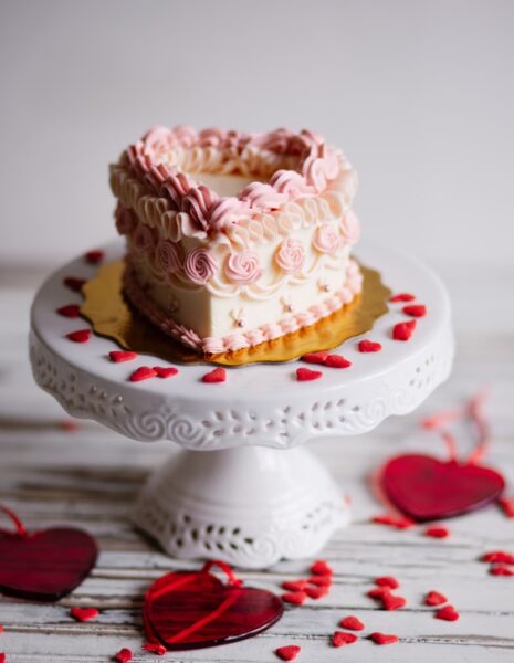 Ein rosaner Kuchen in Herzform steht auf einer Kermaiketagere
