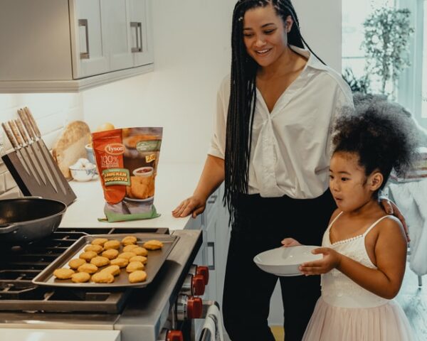 Frau mit kleiner Tochter blicken auf ein Blech mit gebackenen Keksen