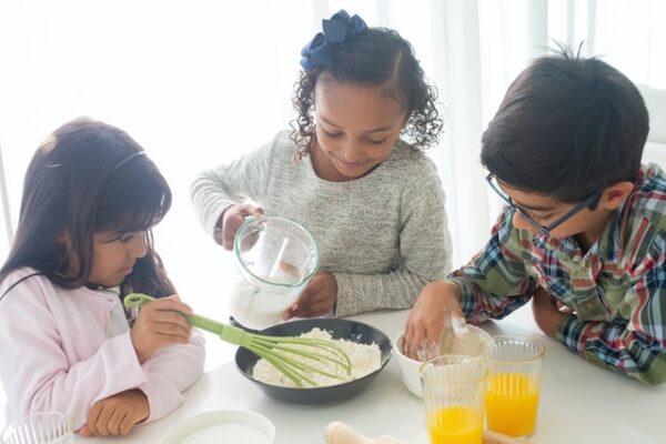 Drei Kinder hantieren mit Mehl und Milch