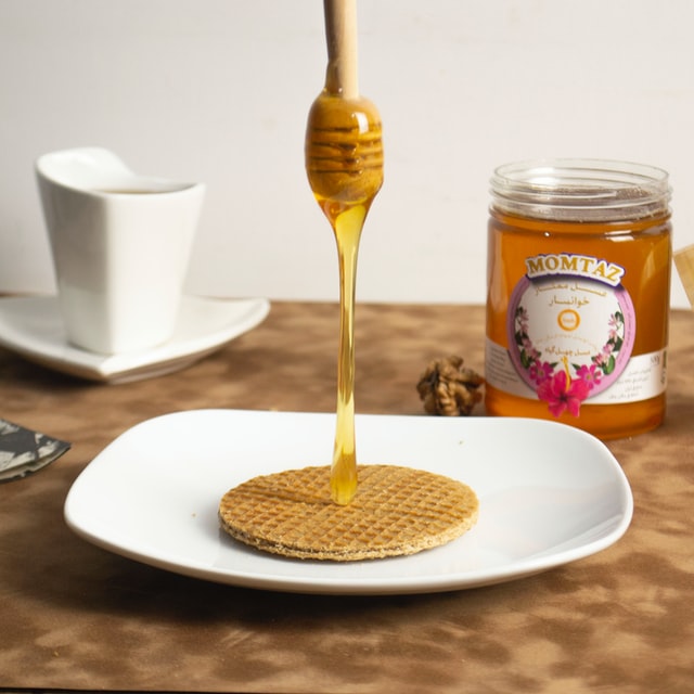 Eine Waffel auf einem Teller, darüber ein Honiglöffel mit herunterfließendem Honig
