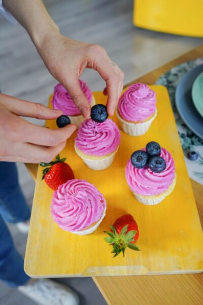 Eine Person dekoriert Cupcakes mit Blaubeeren