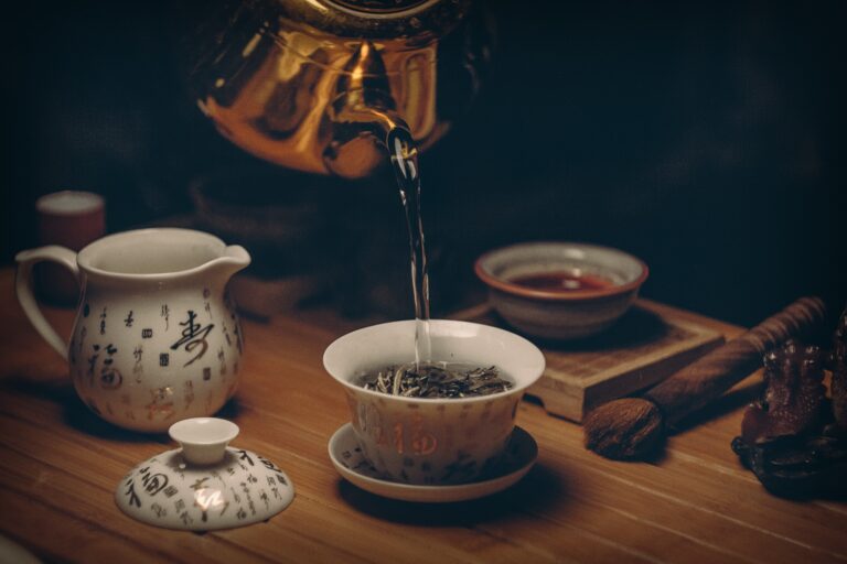 Teekanne, die heißes Wasser in eine Tasse füllt, die mit Teeblättern gefüllt ist