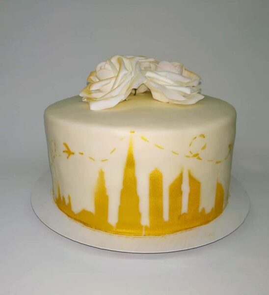 Eine Torte mit einer goldenen Skyline drumherum und Rosen drauf.