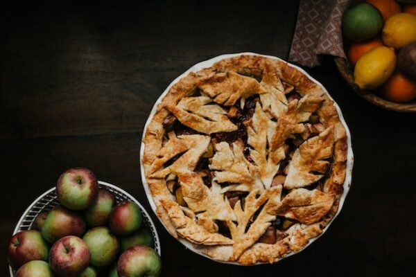 Ein Pie, geschmückt mit Blättern aus Teig und daneben eine Schüssel mit Äpfeln