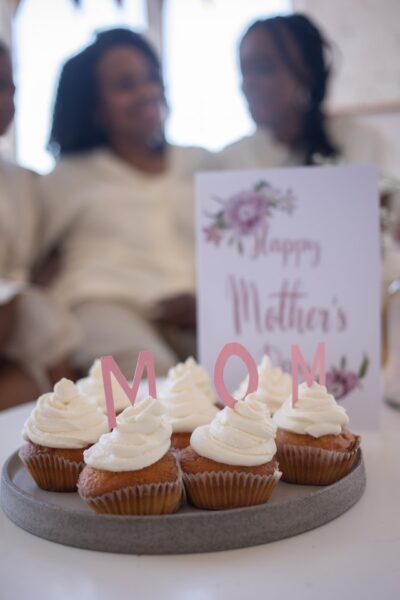 Muffins mit Dekoration: Mom, im Hintergrund Personen und eine Muttertagskarte.