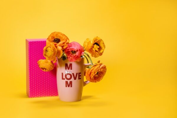 Eine Vase mit Blumen, auf der "love Mom" steht. Dahinter ein pinkes Geschenk