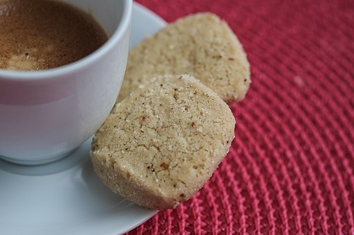 Zwei Heidesand-Kekse liegen auf einem Untersetzer neben einer halb gefüllten Kaffeetasse