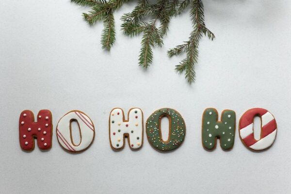 unter einem Tannenzweig liegen weihnachtlich dekorierte Plätzchen in Form von Buchstaben, sie schreiben "Ho Ho Ho"