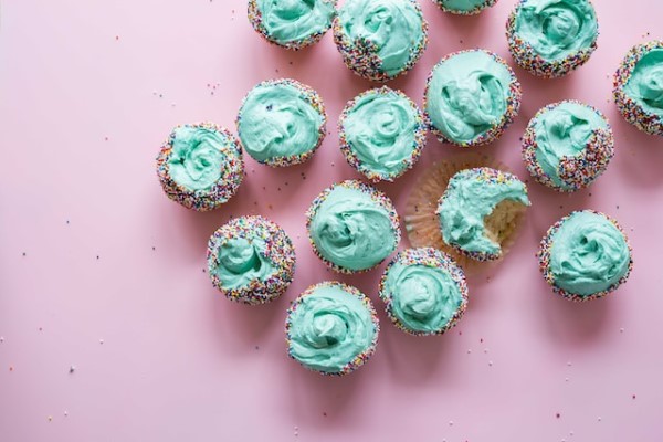 Cupcakes mit hellgrünem Frosting und Zuckerkügelchen auf pinkem Untergrund