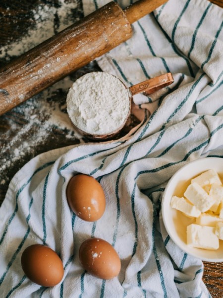Mehl, Eier, Butter und ein Nudelholz liegen neben bzw. auf einem Küchentuch.